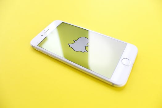 White smartphone displaying Snapchat logo on a bright yellow background, angled view.