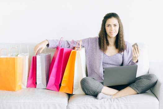 Young woman enjoying online shopping with a laptop and colorful bags on a sofa.