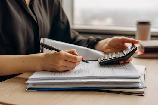 Close-up of person using a calculator with financial documents in an office.